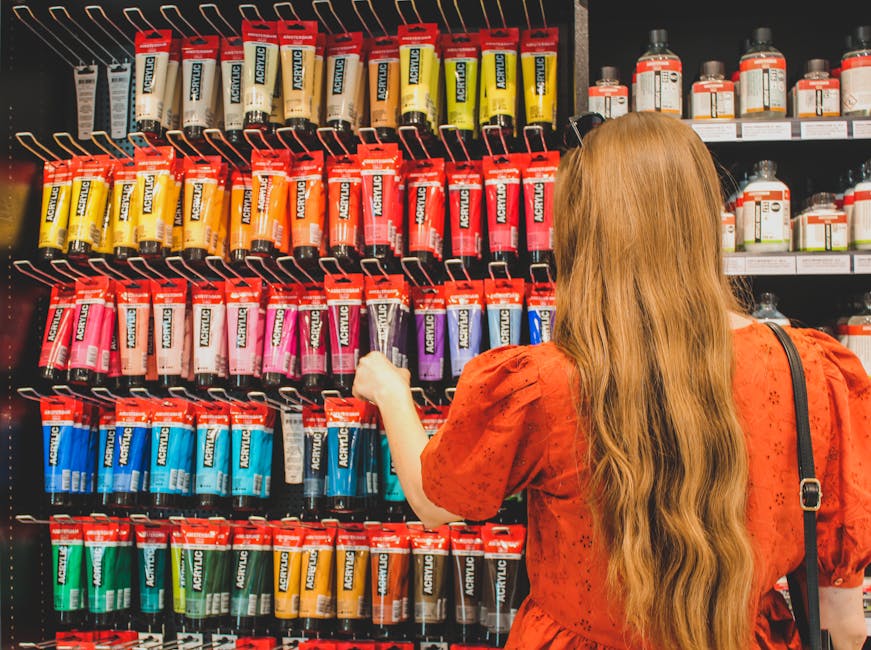 A woman in a red dress selecting acrylic paints from a vibrant display in a Boston art supply store.